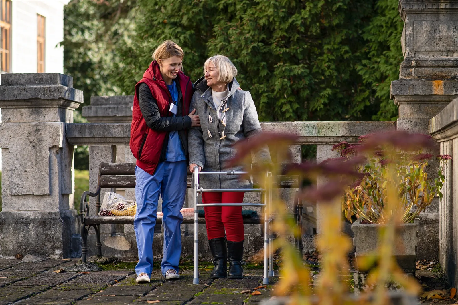 Woman helping an older woman with a walking frame outdoors