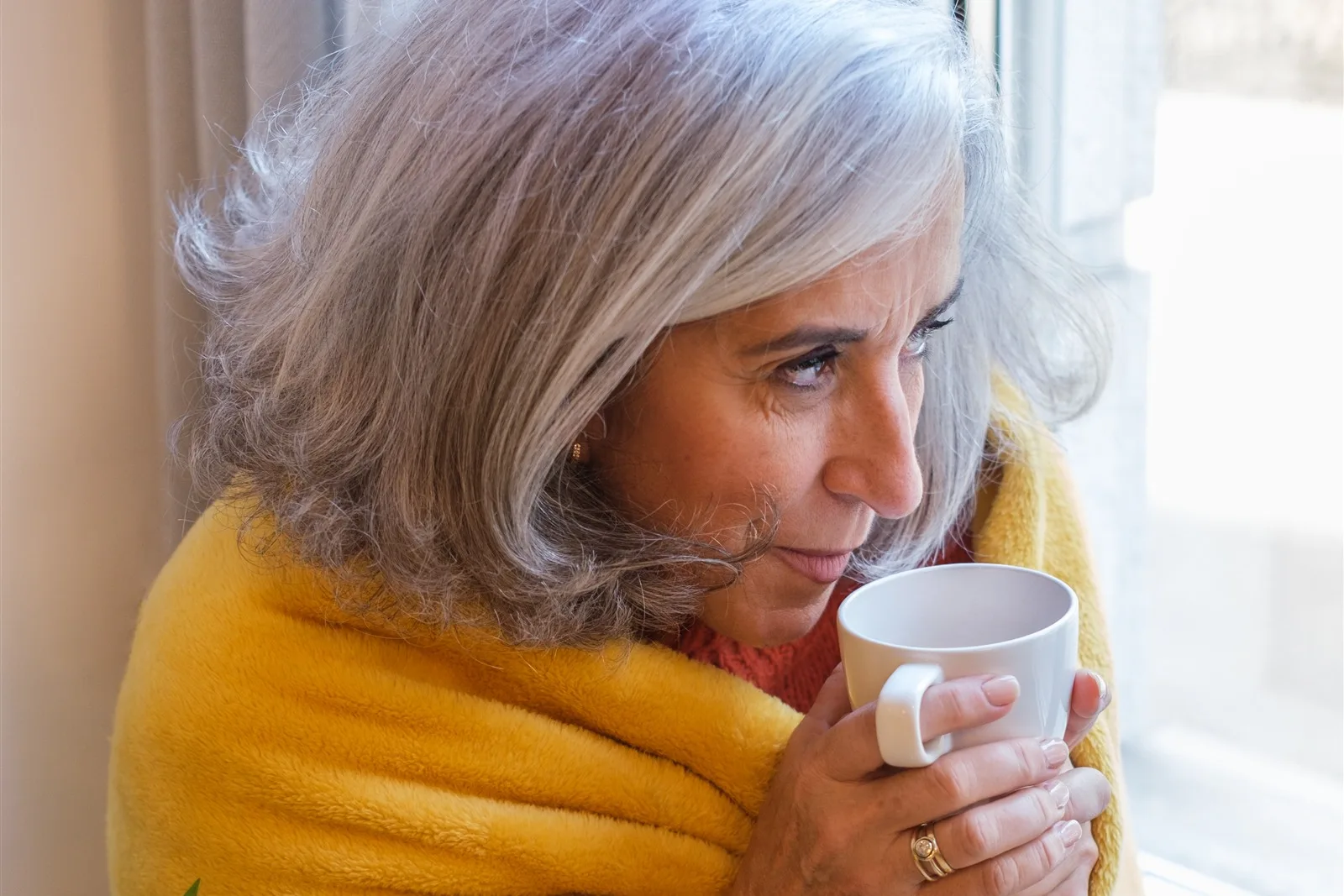 Older woman with a warm drink and blanket by the window