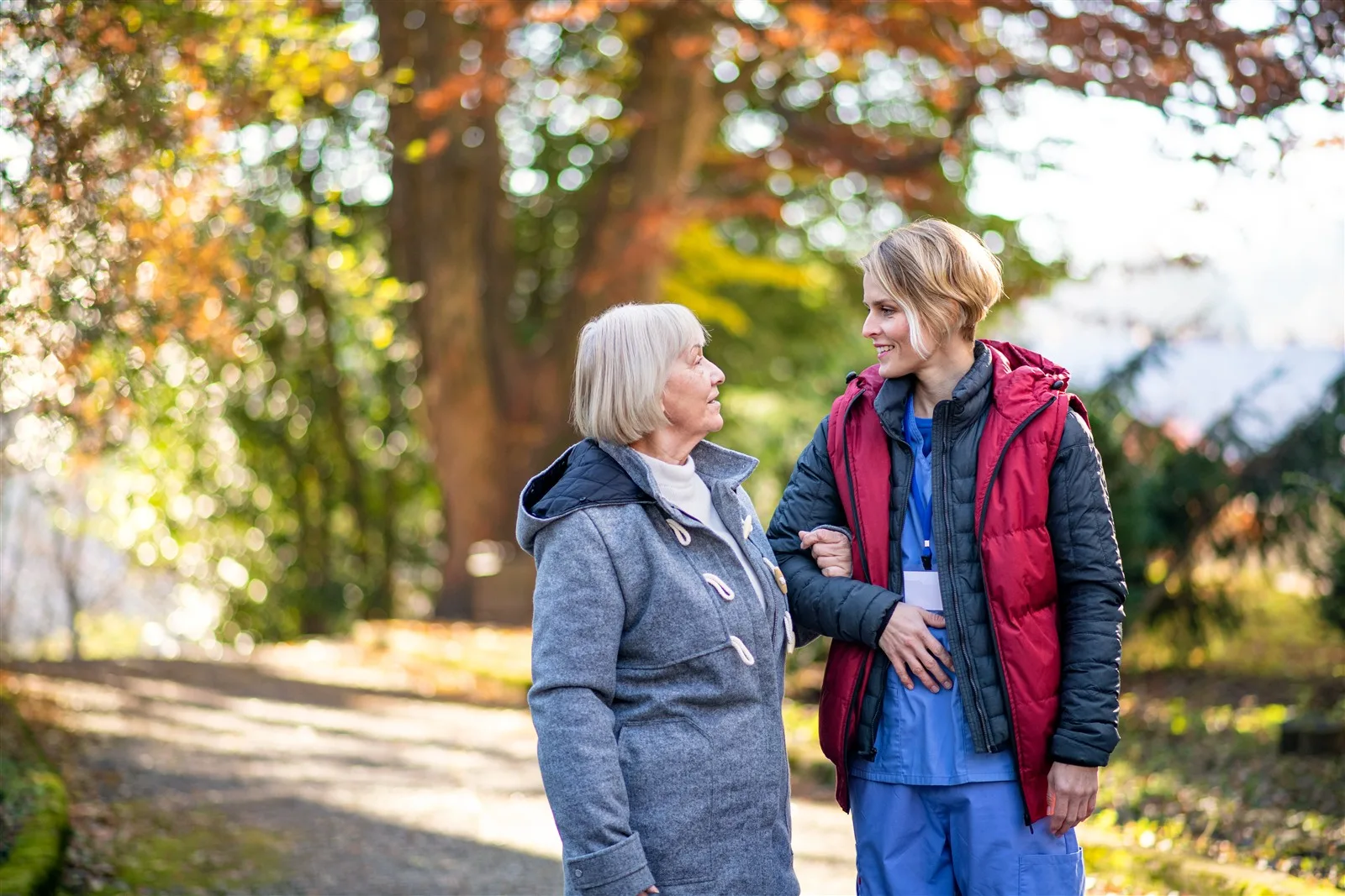 Home Care in Thaxted: Helping You Stay Independent at Home Younger woman walking arm in arm with an older woman in a park